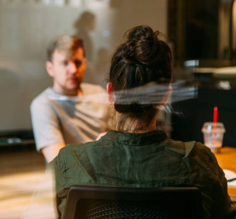 Two people talking across a table, seen through a glass wall